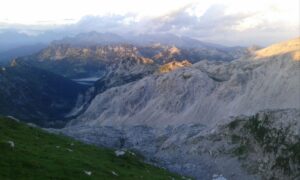 Mountain view of Lake Krn and the surrounding Julian Alps at sunset, showing rocky ridges and distant peaks.